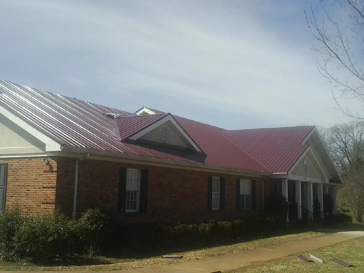 Red metal roof with gabled entries on a long brick building, from a Hail Damage Roof Repair job in Marlow