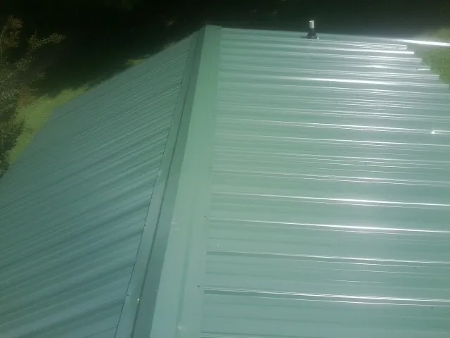 New green metal panels meeting at the ridge of a roof — Flat Roof Repair work by our crew in Marlow
