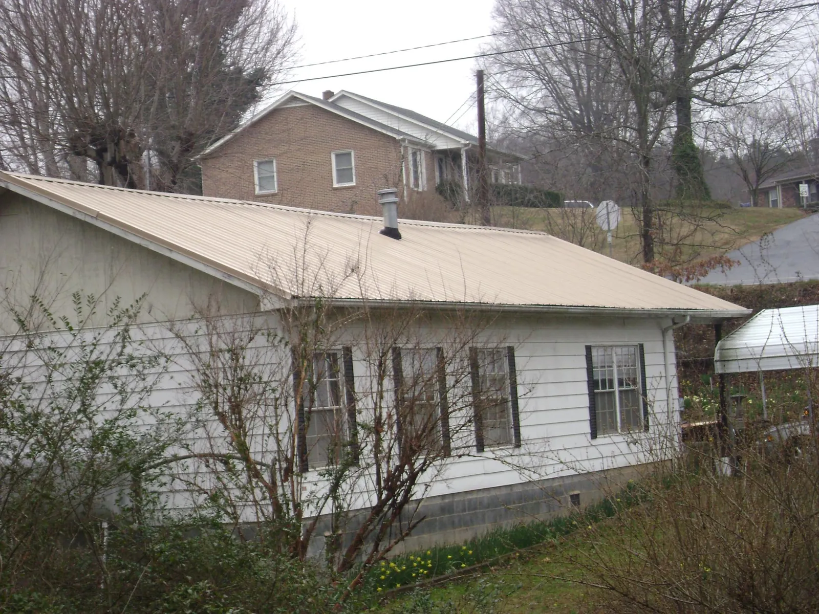 Tan metal roof on a white sided house set into a hillside — Commercial Roofing by Roofing Brothers in Marlow