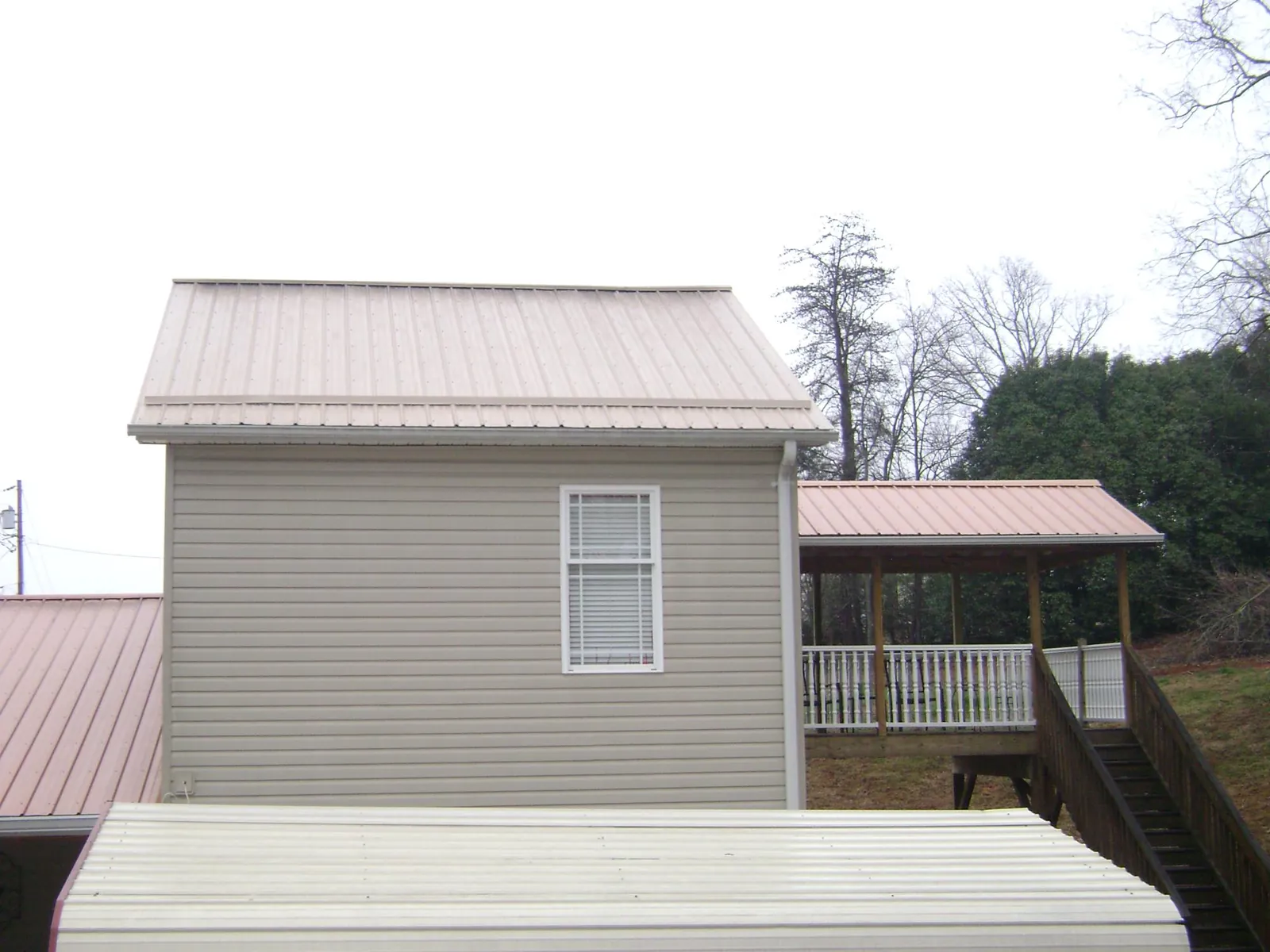 Tan metal roofs on a two story addition and attached porch, from a Roof Replacement job in Marlow